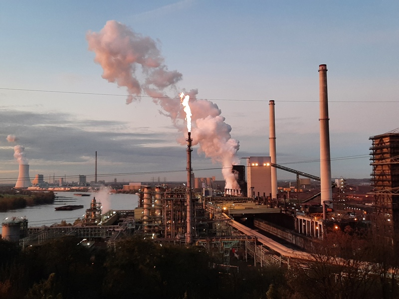 Blick auf den Rhein und die Kokerei Schwelgern mit Wasserdampf und Werksbeleuchtung.
